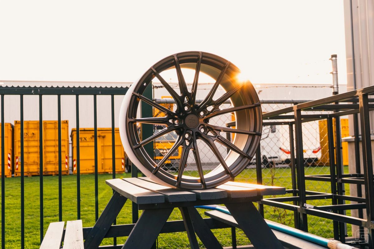 Dark multi-spoke alloy wheel displayed outdoors in warm sunset light.